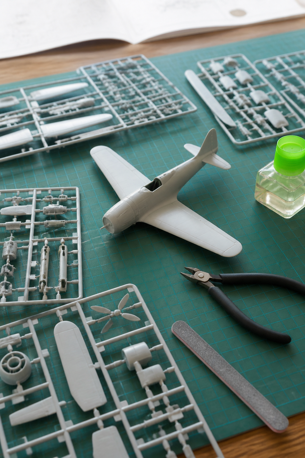 An unbuilt plastic aircraft kit laid out on a cutting mat with sprue nippers, a sanding stick and liquid cement