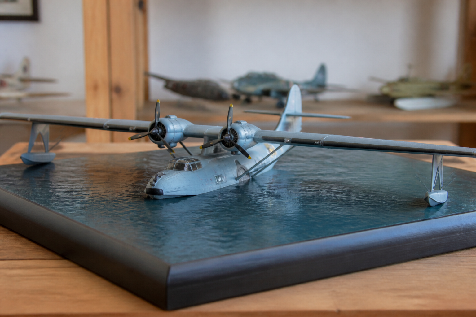 A twin-engine flying boat model with wingtip floats resting on a display base painted as calm water
