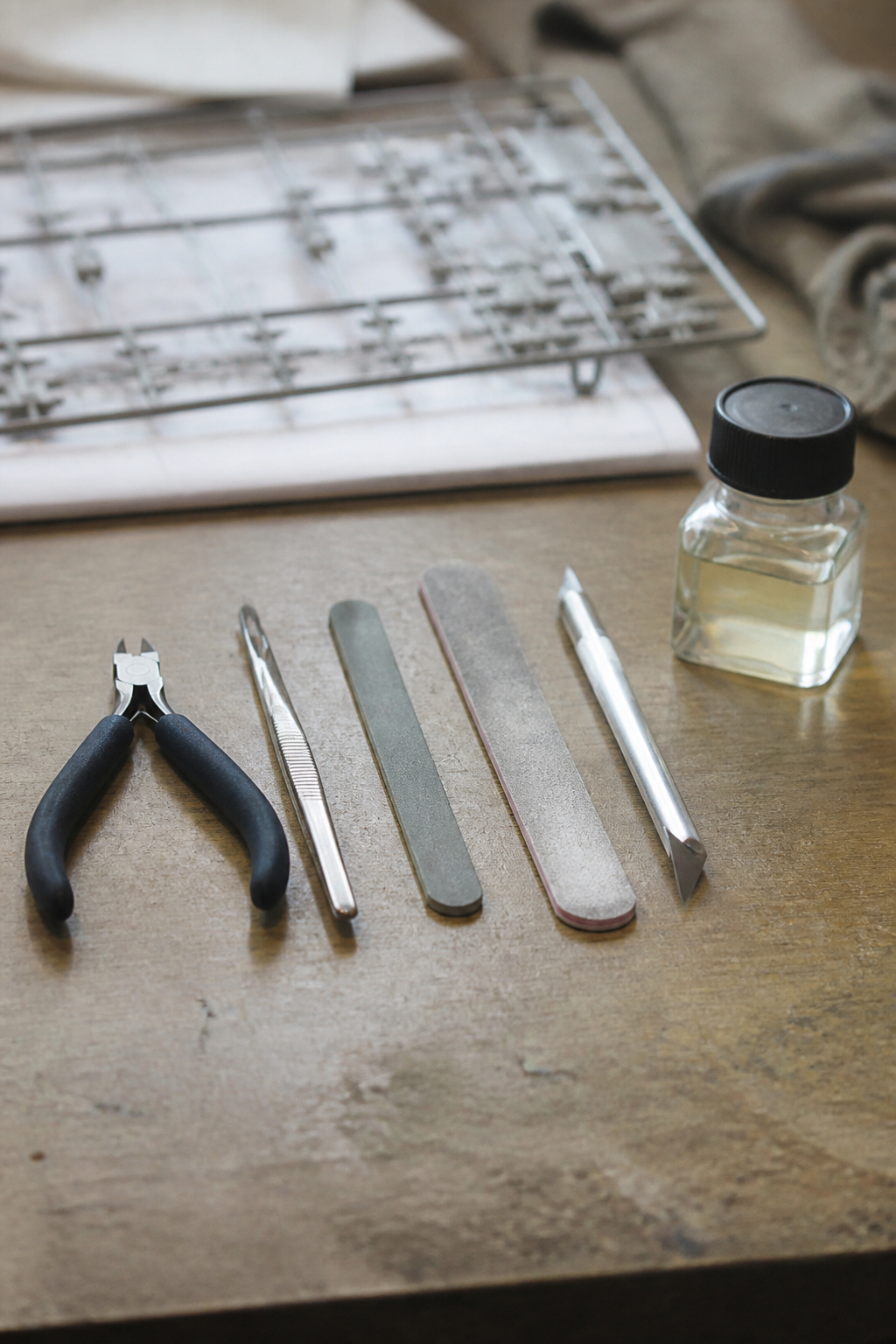 Modelling tools laid in a row: sprue nippers, tweezers, sanding sticks, a scalpel and a pot of liquid cement