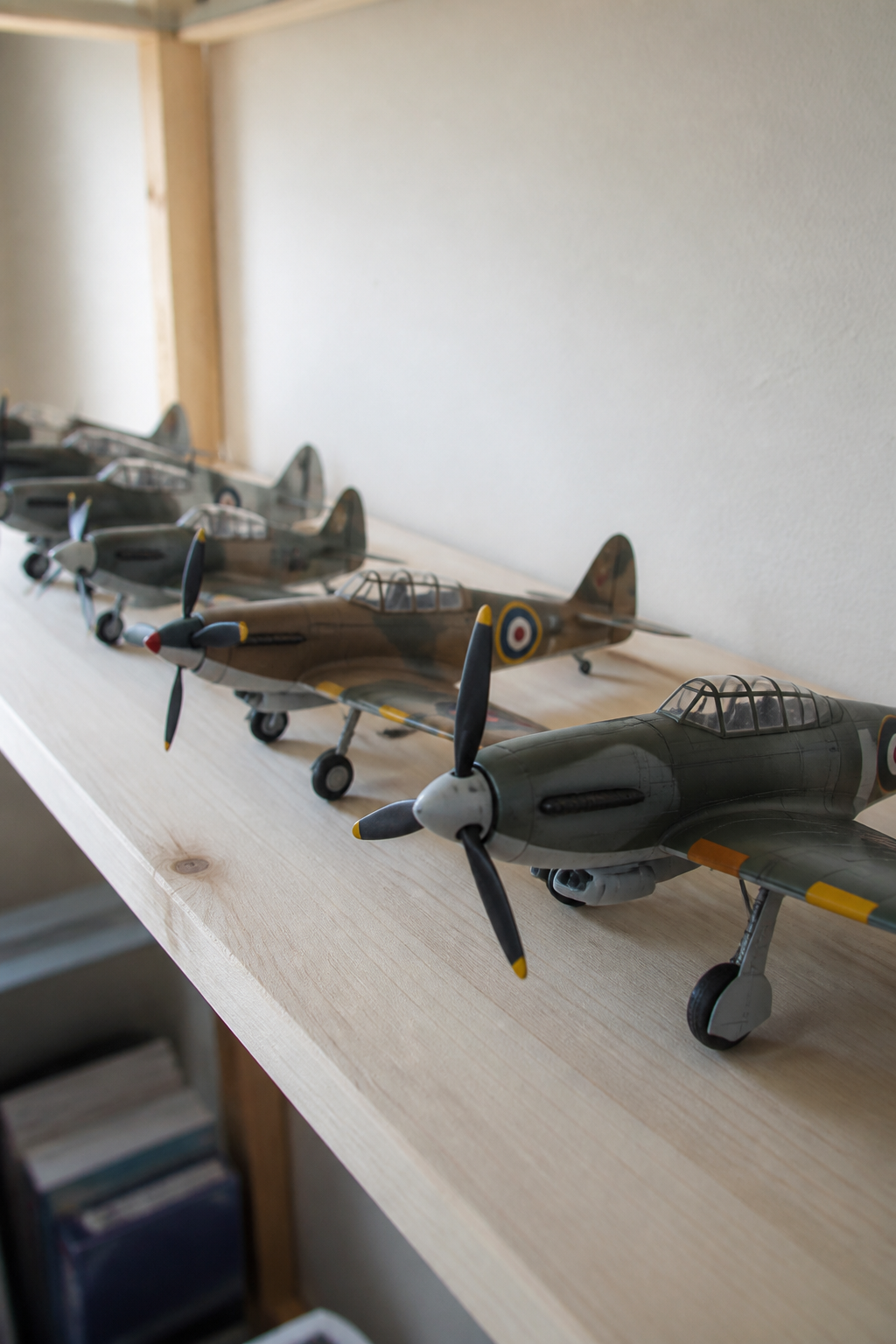 A row of finished propeller aircraft models of the same scale on a pale wooden shelf, lit from the left
